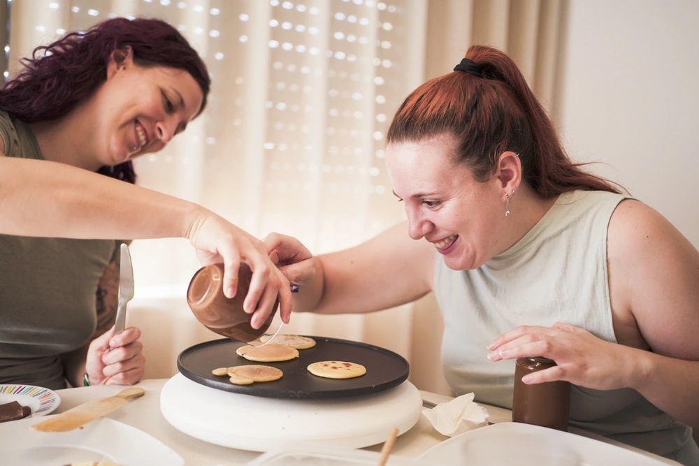 woman helping a a disabled woman in cooking pancakes